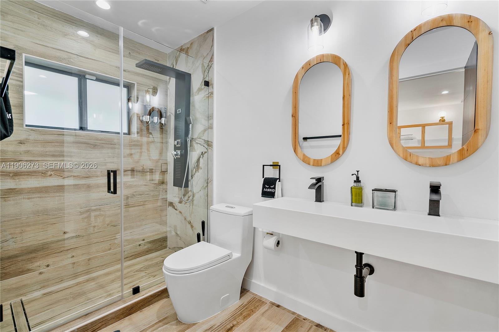 A modern bathroom features a glass-enclosed shower, a white floating vanity, and two oval mirrors — 256 NW 57th St, Miami FL 33127, MIAMI, FL