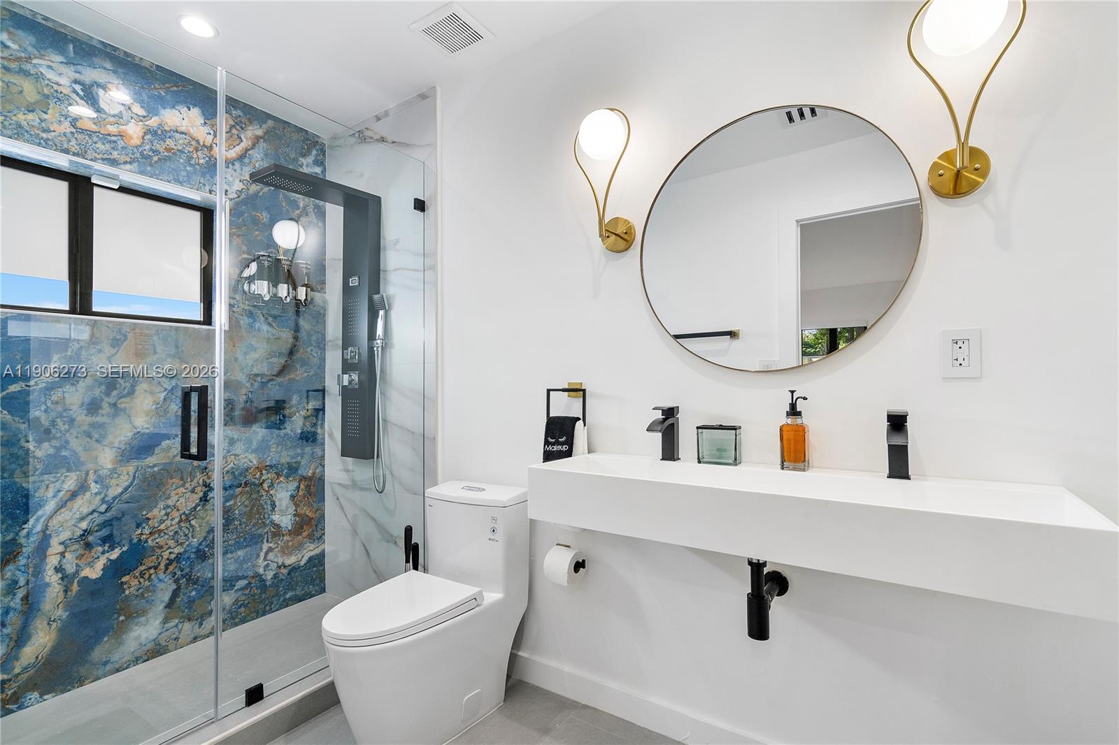 A modern bathroom features a blue marble-tiled shower, a floating white vanity, and gold sconces — 256 NW 57th St, Miami FL 33127, MIAMI, FL
