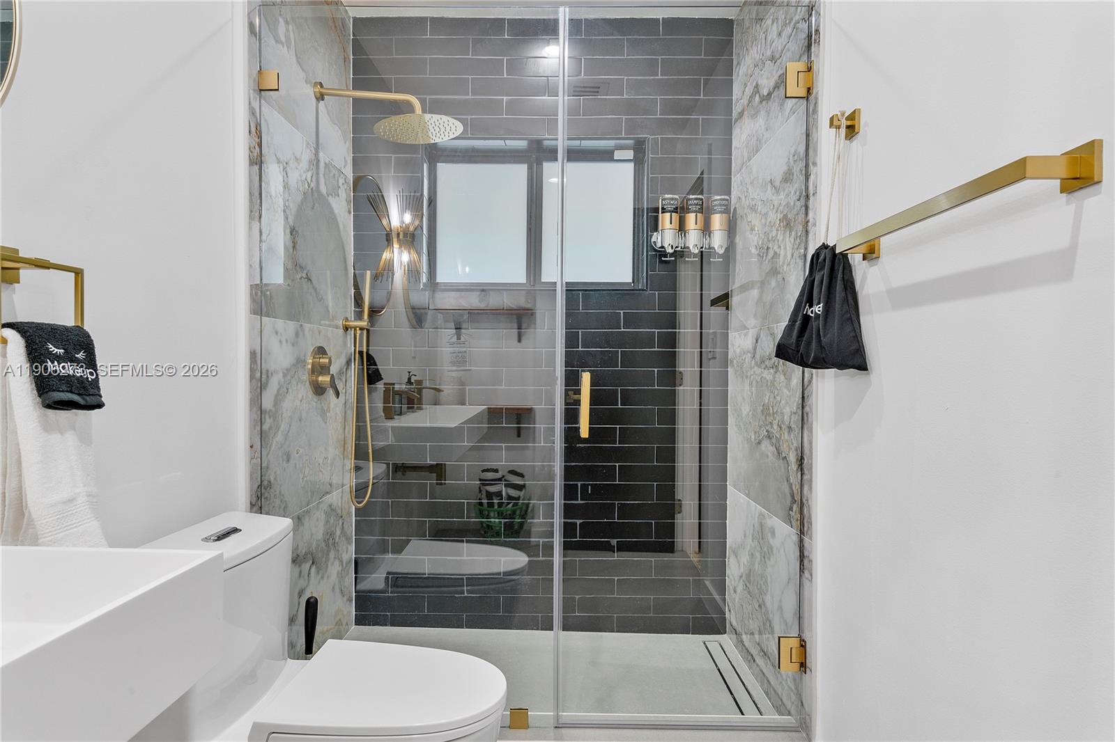 A modern bathroom features a glass-enclosed shower with dark subway tiles and gold fixtures — 256 NW 57th St, Miami FL 33127, MIAMI, FL
