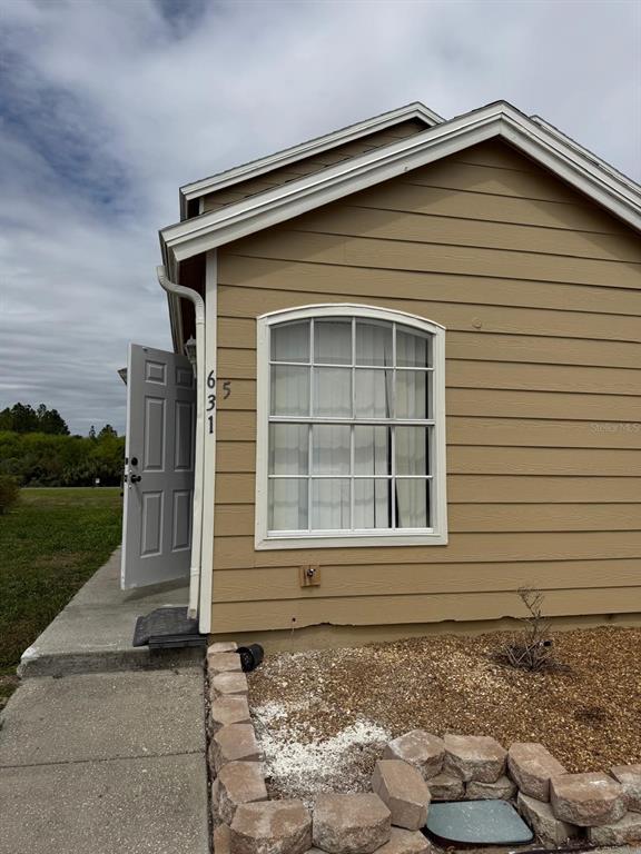 The exterior of a tan house features a white door, a window, and stone landscaping — 631 WASHINGTON PALM LOOP, DAVENPORT, FL