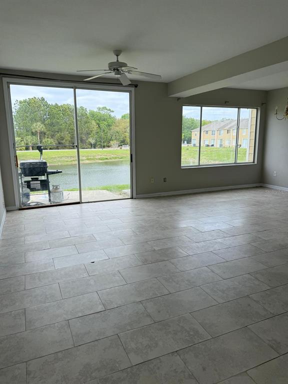 An empty living area features light-colored tile flooring, a ceiling fan, and large sliding doors — 631 WASHINGTON PALM LOOP, DAVENPORT, FL