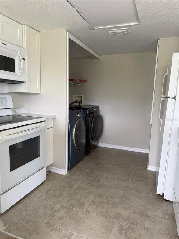 A kitchen with white appliances, light-colored cabinets, and a laundry area with two machines — 631 WASHINGTON PALM LOOP, DAVENPORT, FL