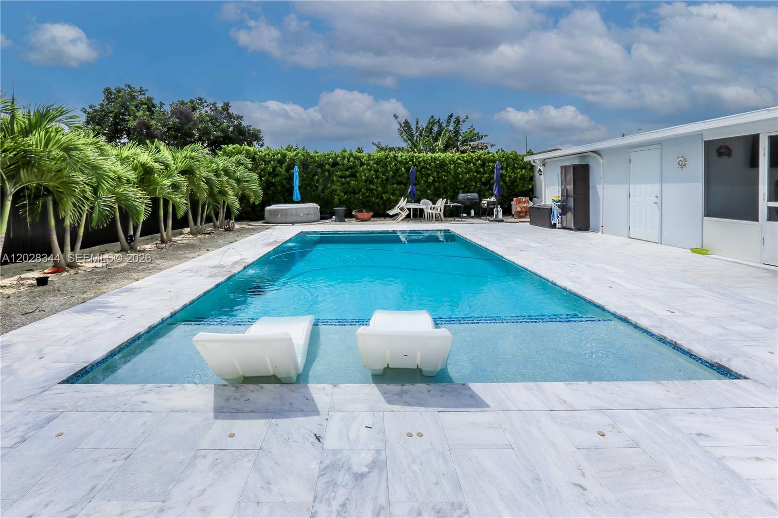 A rectangular swimming pool with a tanning ledge and two lounge chairs sits on a patio — 12100 SW 181st Ter, Miami FL 33177, MIAMI, FL