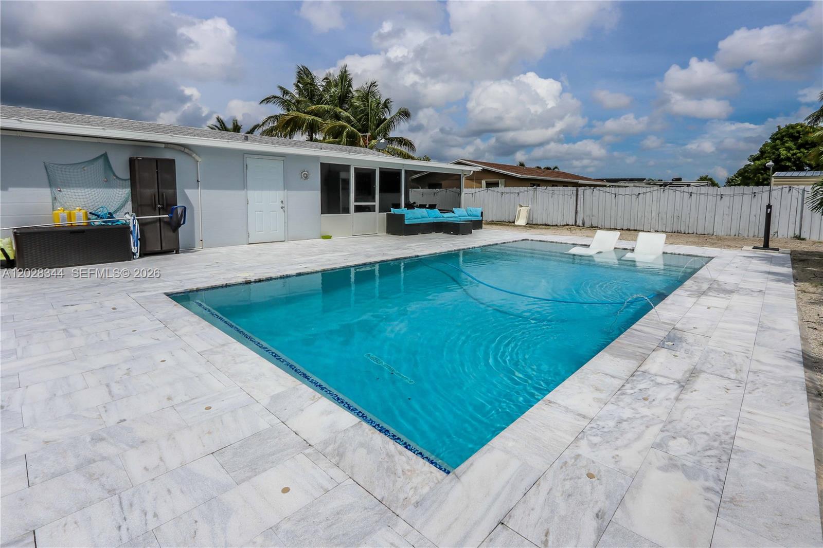 A rectangular swimming pool sits in a paved backyard next to a single-story house — 12100 SW 181st Ter, Miami FL 33177, MIAMI, FL