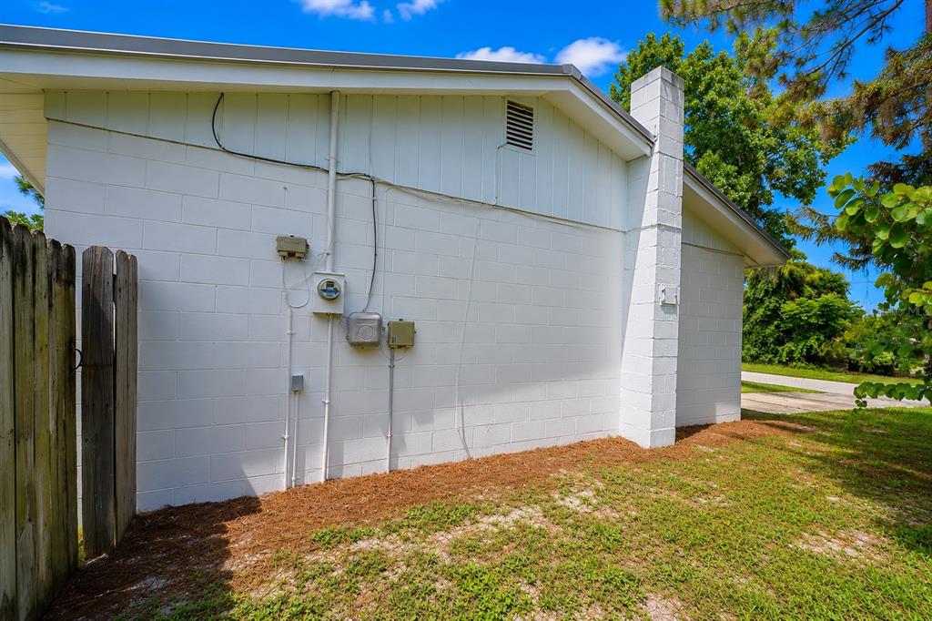 The exterior side wall of a white concrete block house features a chimney and utilities — 2824 YULE TREE DRIVE, EDGEWATER, FL