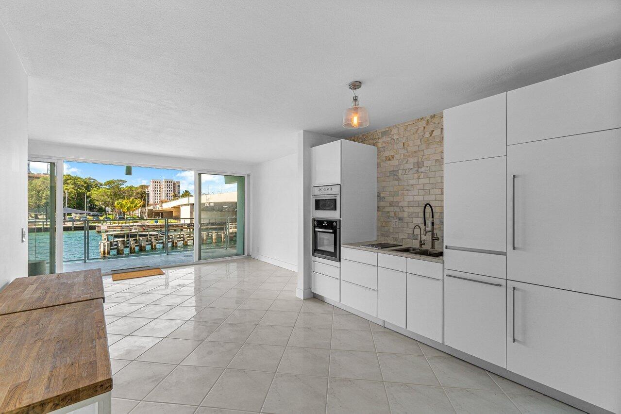 A modern kitchen with white cabinetry and a stone backsplash overlooks a waterfront balcony — 65 SE Spanish Trail # 2020, Boca Raton FL 33432, BOCA RATON, FL