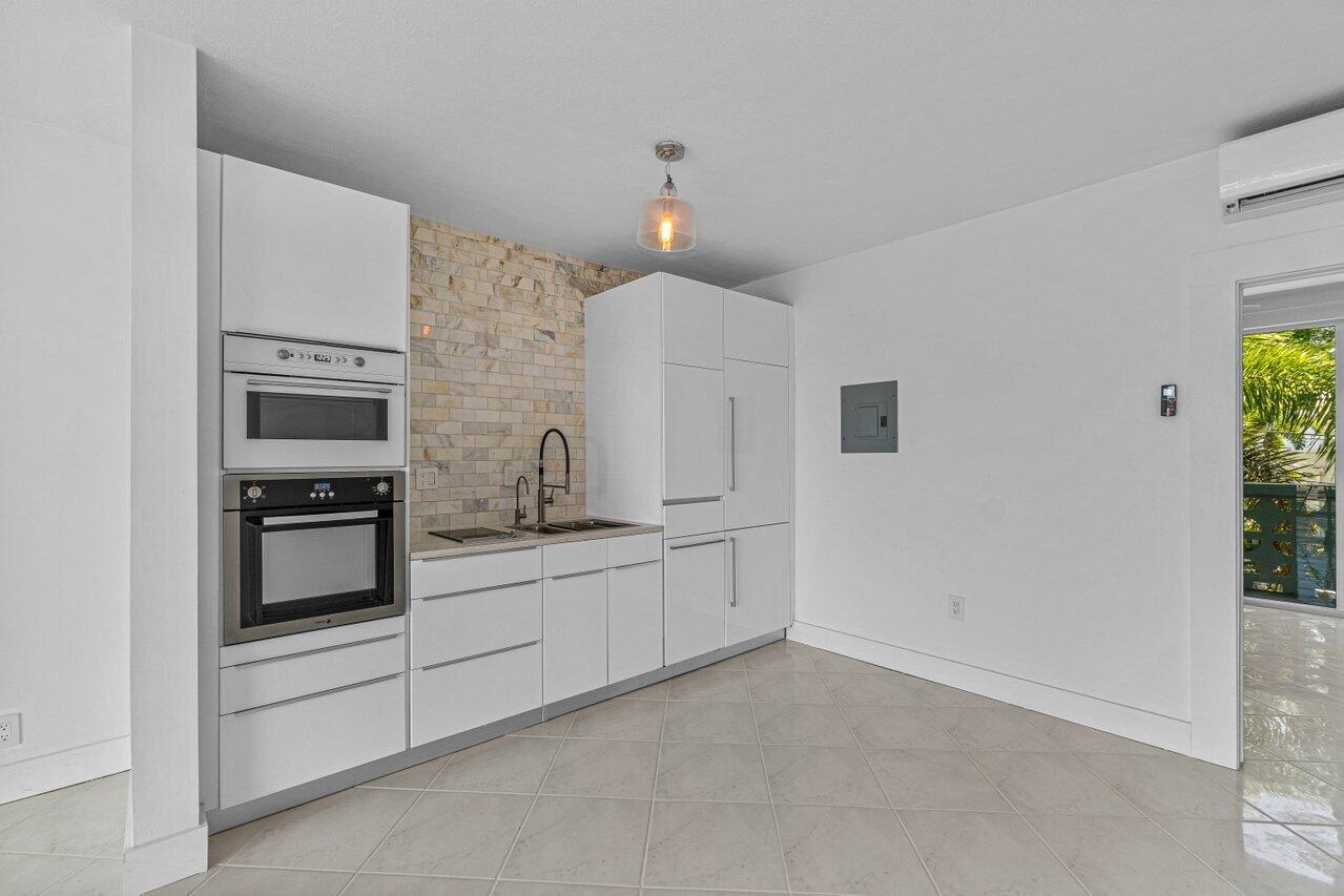 A modern kitchen features white cabinetry, a stone backsplash, and built-in stainless steel appliances — 65 SE Spanish Trail # 2020, Boca Raton FL 33432, BOCA RATON, FL