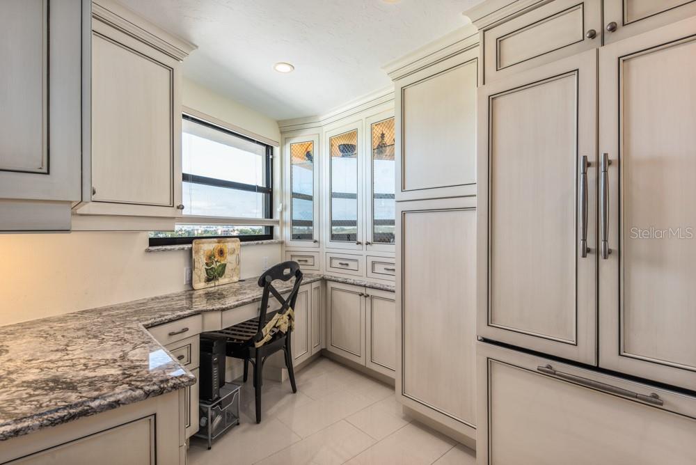 A kitchen features light-colored cabinetry, granite countertops, a built-in desk area, and a large refrigerator — 5770 MIDNIGHT PASS ROAD UNIT 605, SARASOTA, FL