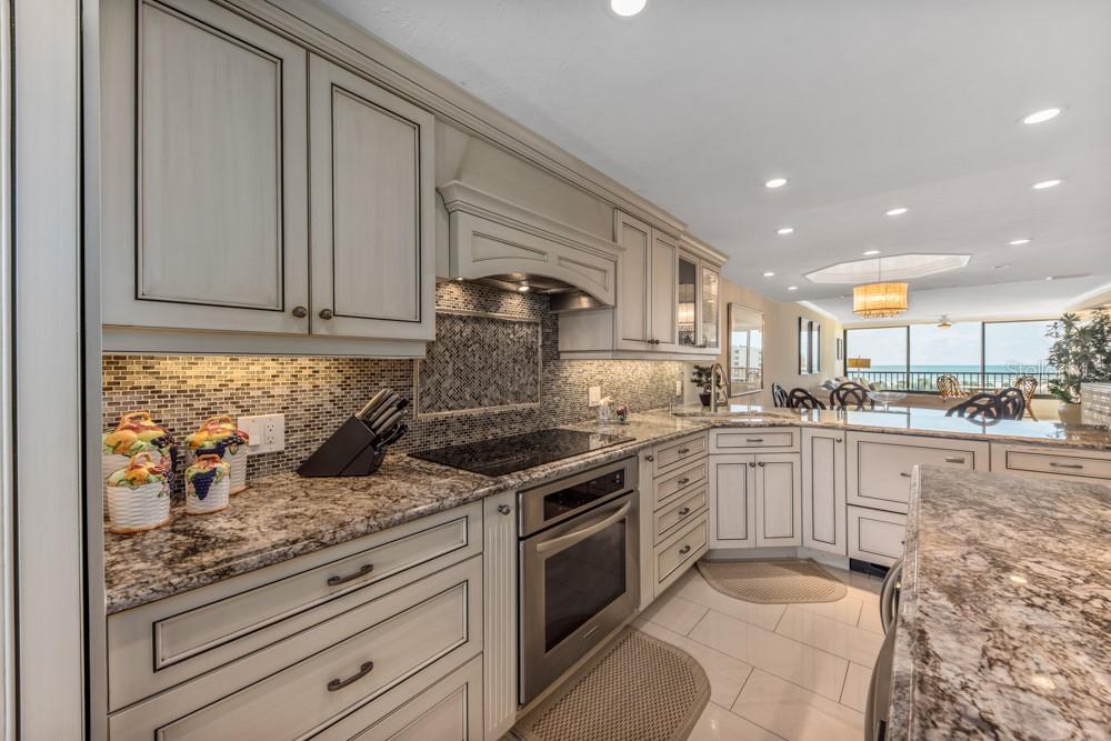 A kitchen features light-colored cabinetry, granite countertops, a tiled backsplash, and stainless steel appliances — 5770 MIDNIGHT PASS ROAD UNIT 605, SARASOTA, FL