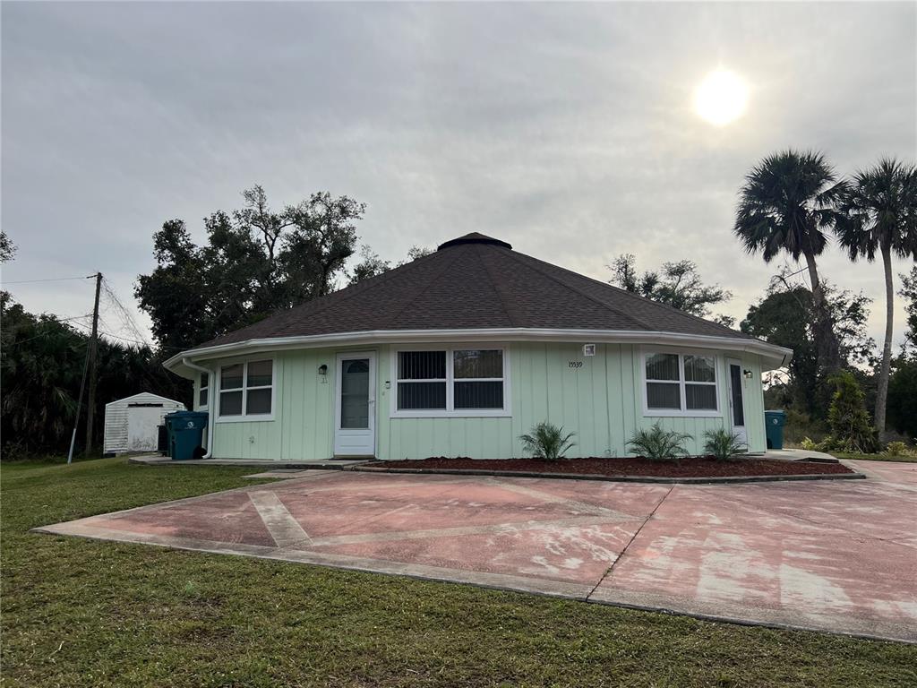 A round, light green house with a dark shingled roof and a concrete driveway — 15539 CHAMBERLAIN BOULEVARD, PORT CHARLOTTE, FL