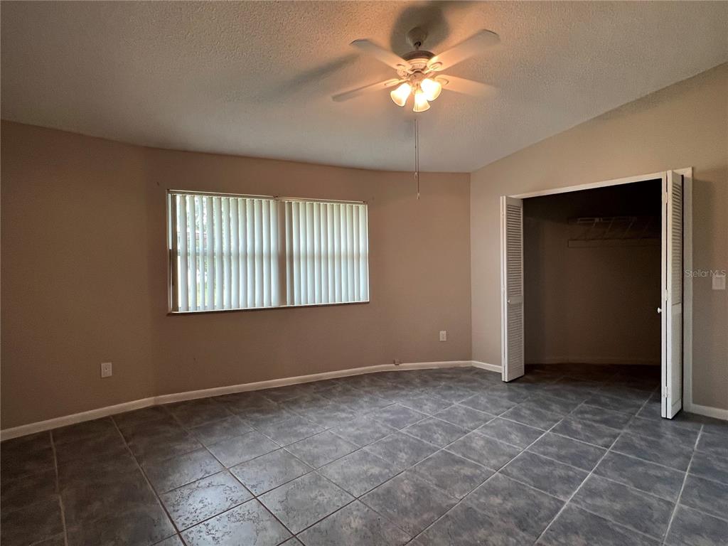 A bedroom features gray tile flooring, a ceiling fan, a window with blinds, and a closet — 15539 CHAMBERLAIN BOULEVARD, PORT CHARLOTTE, FL