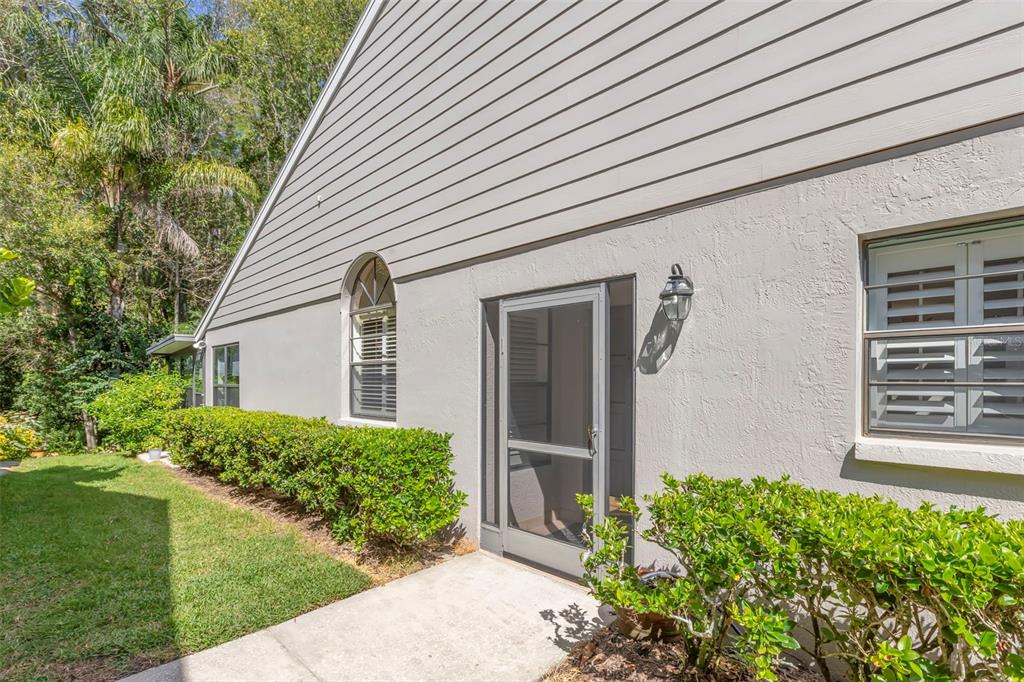 A side view of a house exterior featuring a screen door, windows, and landscaping — 4060 SALEM SQUARE PARKWAY, PALM HARBOR, FL