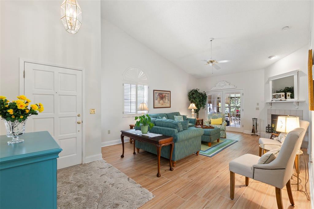 A bright living room features vaulted ceilings, light wood-look tile flooring, and a stone fireplace — 4060 SALEM SQUARE PARKWAY, PALM HARBOR, FL