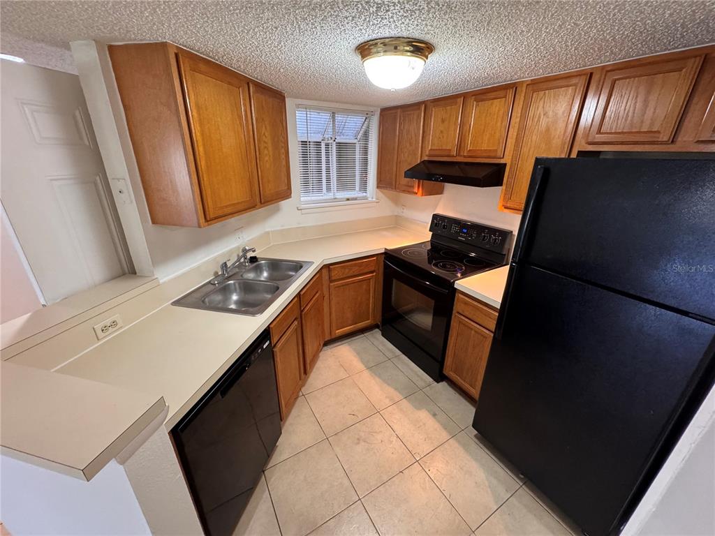A kitchen features wood cabinets, black appliances, a double sink, and light-colored tile flooring — 1916 LAKE ATRIUMS CIRCLE UNIT 40, ORLANDO, FL