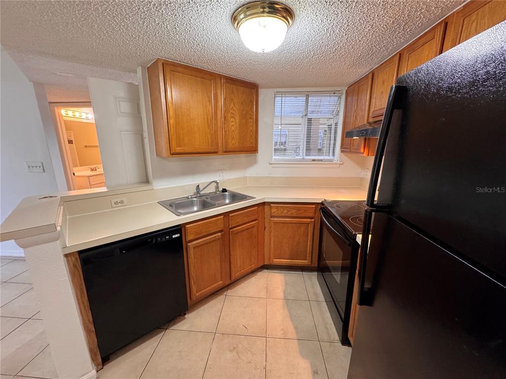A kitchen features wood cabinets, black appliances, a double sink, and light-colored tile flooring — 1916 LAKE ATRIUMS CIRCLE UNIT 40, ORLANDO, FL