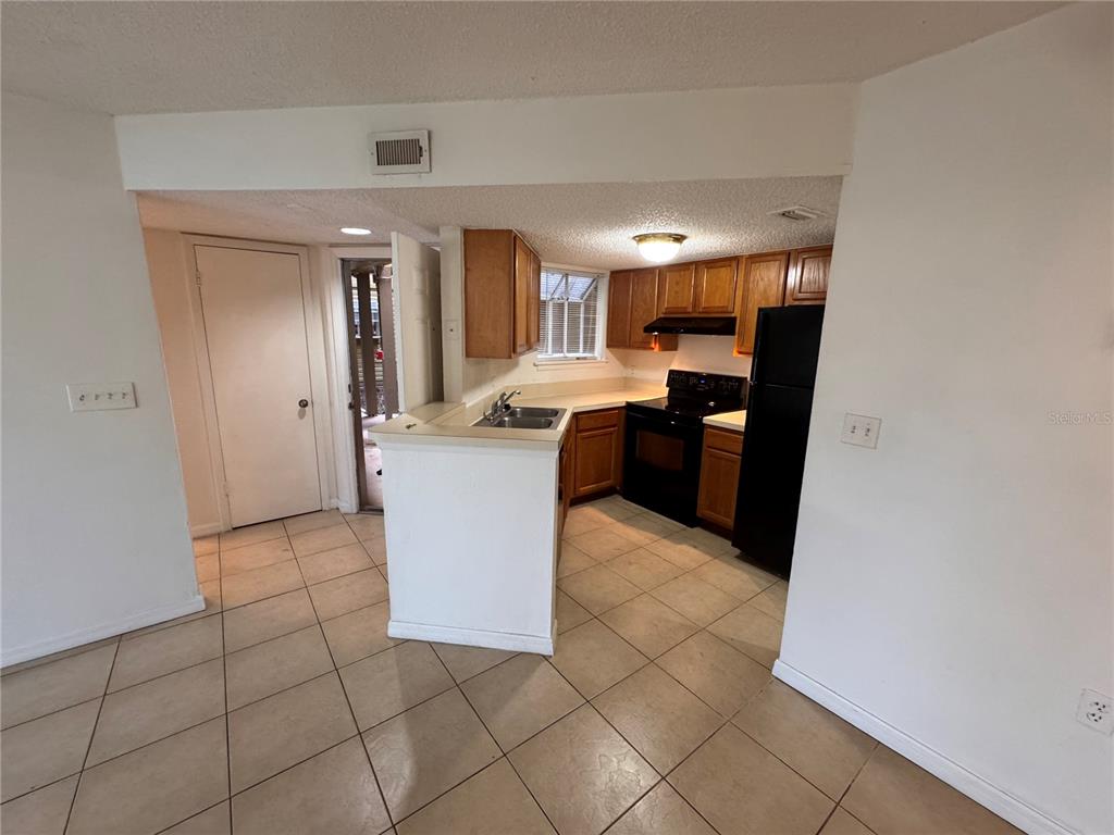 A kitchen features wood cabinets, black appliances, a tile floor, and a breakfast bar — 1916 LAKE ATRIUMS CIRCLE UNIT 40, ORLANDO, FL