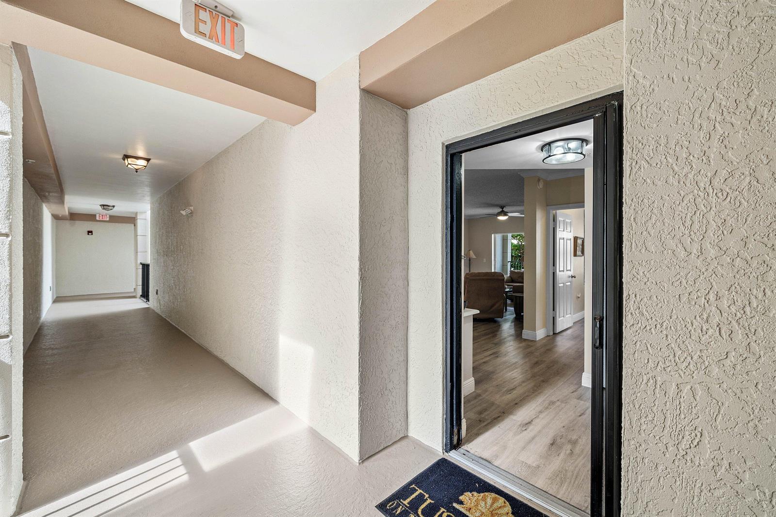 An open doorway leads from a beige outdoor hallway into a home with wood-look flooring — 4307 Tuscany Way, Boynton Beach FL 33435, BOYNTON BEACH, FL