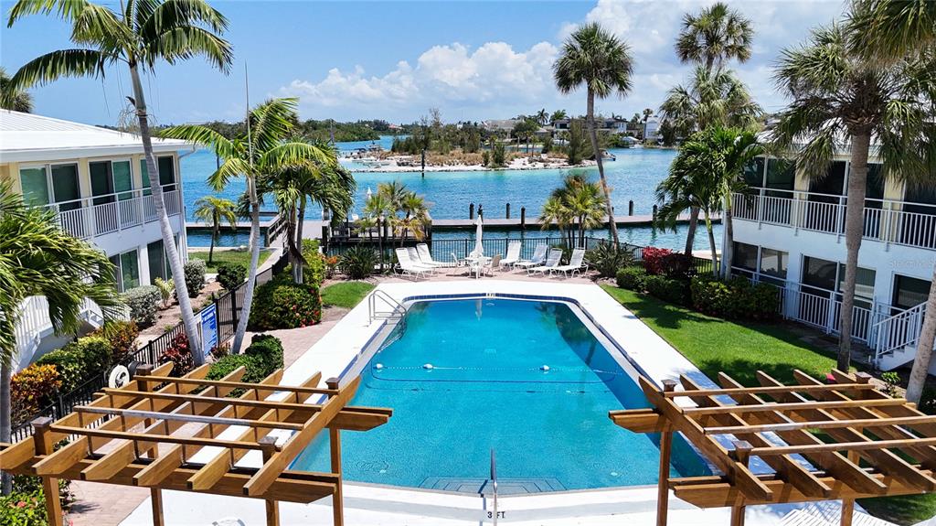 An elevated view of a swimming pool between two buildings with palm trees and water — 999 INLET CIRCLE UNIT B104, VENICE, FL