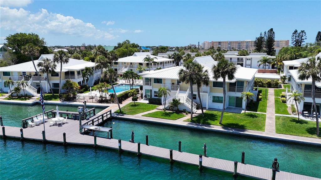 An aerial view shows multi-story waterfront townhomes with white roofs, palm trees, and a wooden dock — 999 INLET CIRCLE UNIT B104, VENICE, FL
