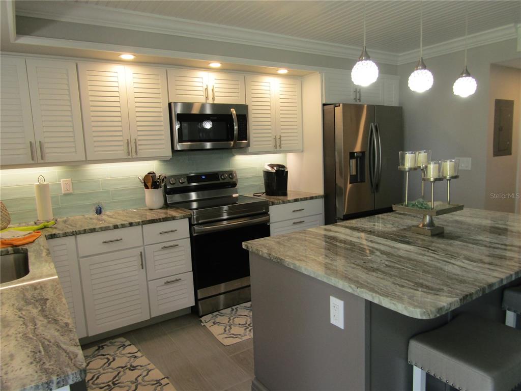 A kitchen features white louvered cabinets, granite countertops, stainless steel appliances, and a central island — 999 INLET CIRCLE UNIT B104, VENICE, FL