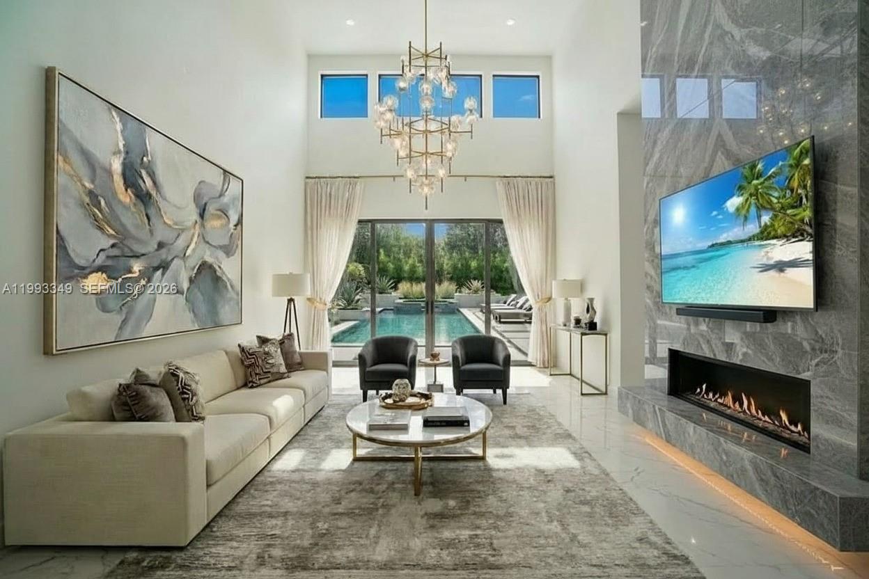 A modern living room features a high ceiling, fireplace, large wall art, and pool view — 680 NW 33rd St, Oakland Park FL 33309, OAKLAND PARK, FL
