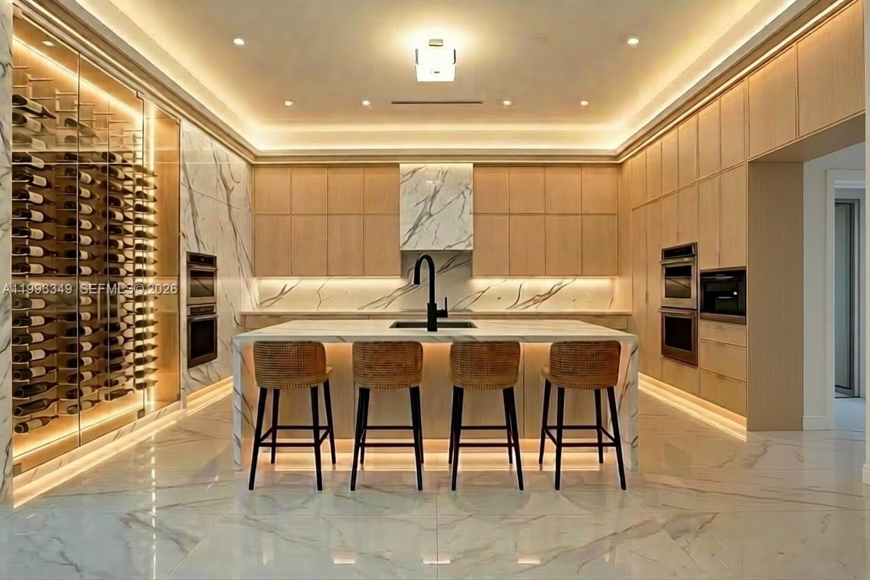 A modern kitchen features light wood cabinetry, marble surfaces, a wine wall, and a central island — 680 NW 33rd St, Oakland Park FL 33309, OAKLAND PARK, FL