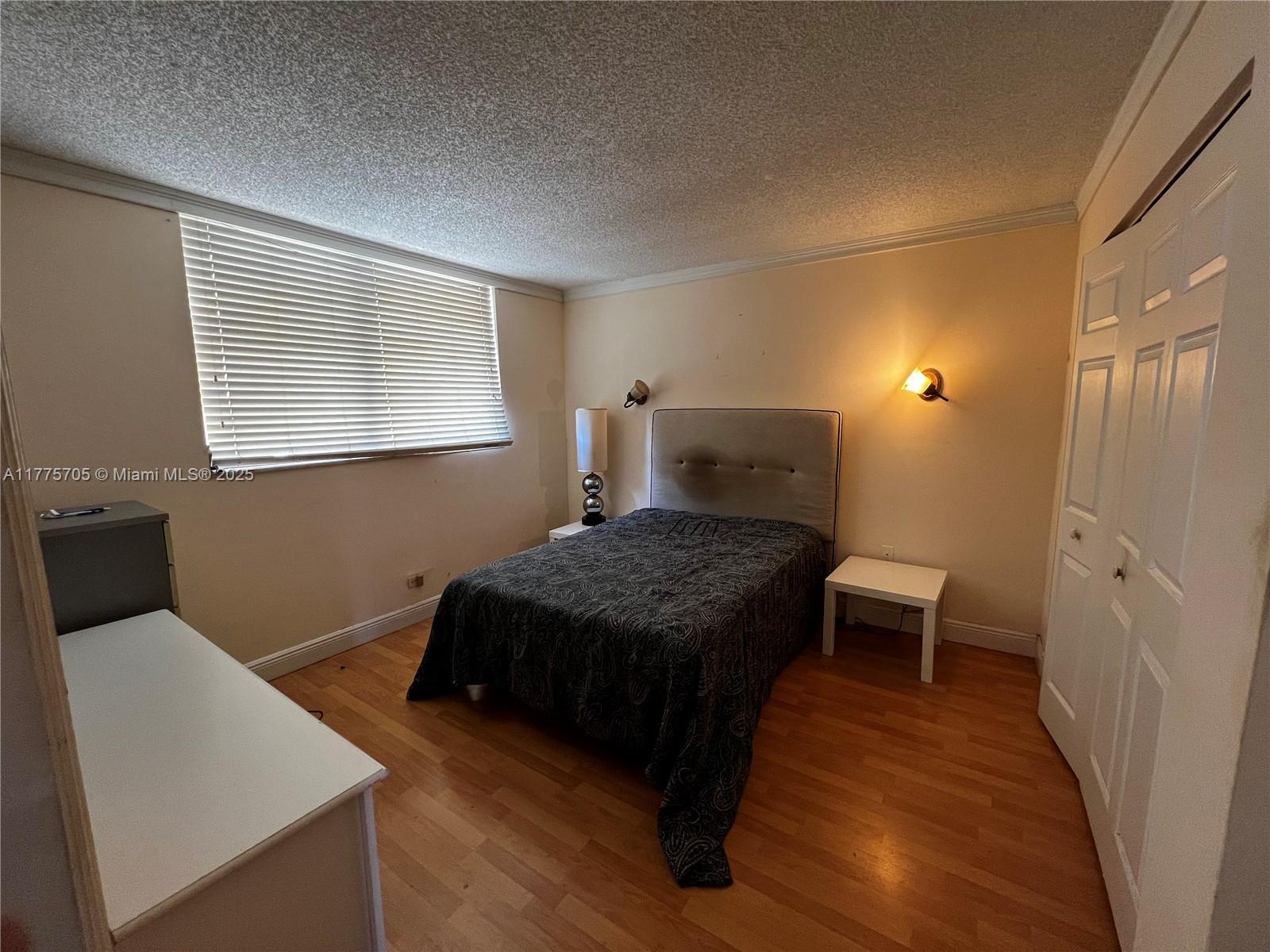 A bedroom features a bed with a grey headboard, wood flooring, and two wall-mounted lamps — 447 NE 195th St # 309, Miami FL 33179, MIAMI, FL