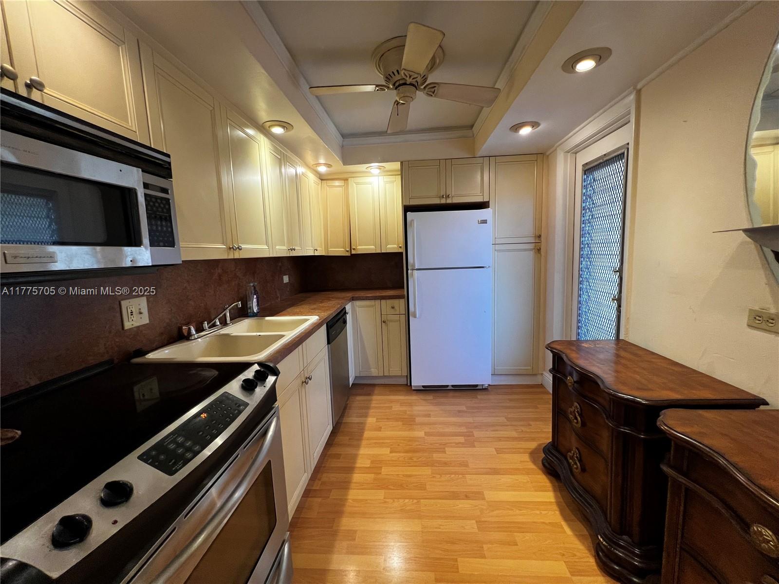 A kitchen features light-colored cabinets, a white refrigerator, stainless steel appliances, and wood flooring — 447 NE 195th St # 309, Miami FL 33179, MIAMI, FL