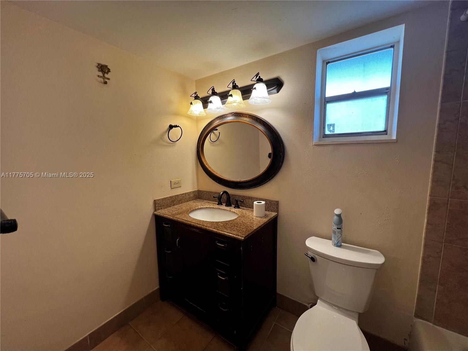 A bathroom features a dark wood vanity with a granite countertop, oval mirror, and toilet — 447 NE 195th St # 309, Miami FL 33179, MIAMI, FL