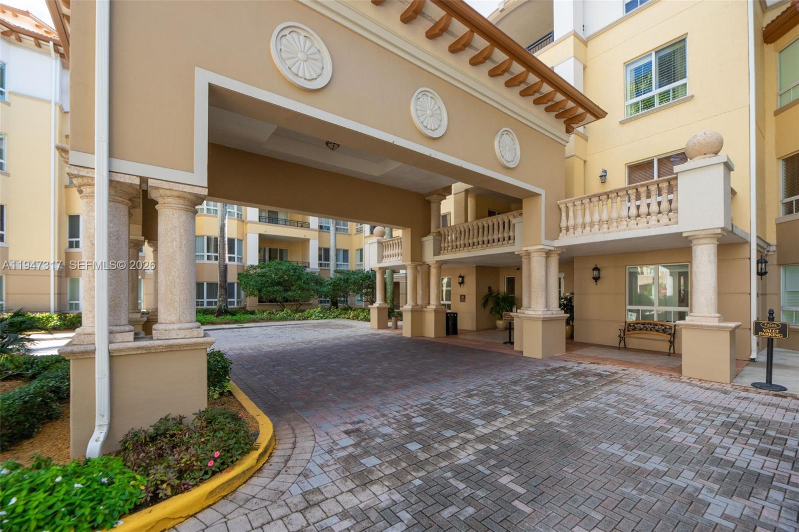 A paved driveway leads under a covered porte-cochère entrance of a multi-story beige building — 16101 Emerald Estates Dr # 250, Weston FL 33331, WESTON, FL