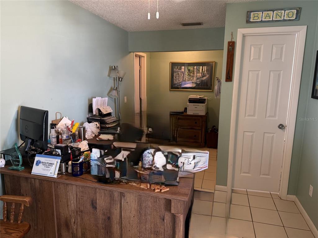 A home office features a wooden desk, a computer, and a door labeled "BANO — 104 S 4TH STREET UNIT 104, FLAGLER BEACH, FL