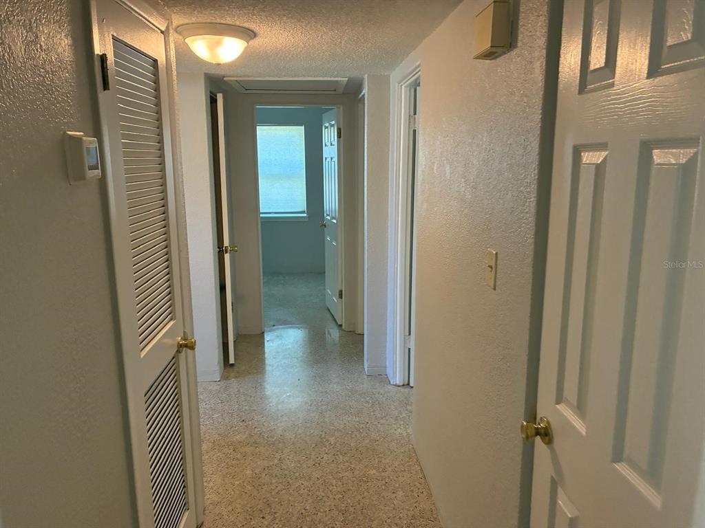 A hallway with white walls, a louvered door, and light-colored tile flooring leads to a bedroom — 4390 68TH STREET N, ST PETERSBURG, FL
