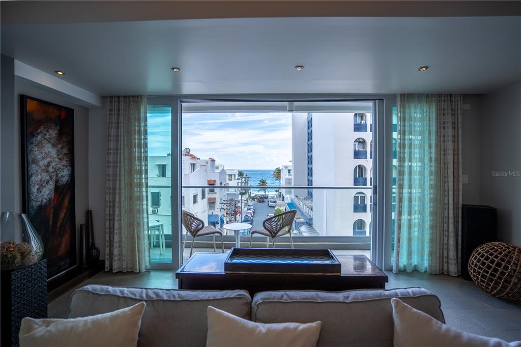 A living room with a sofa faces a balcony overlooking a street and the ocean — 1124 ASHFORD AVENUE UNIT 5B, SAN JUAN, PR