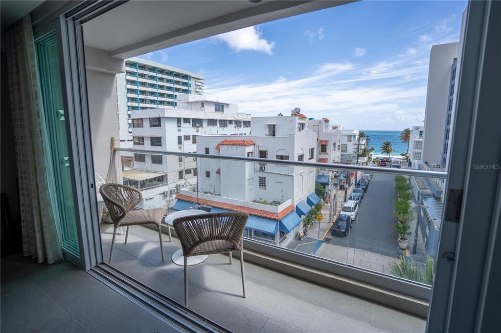 A balcony with two chairs overlooks a street leading to the ocean and nearby buildings — 1124 ASHFORD AVENUE UNIT 5B, SAN JUAN, PR