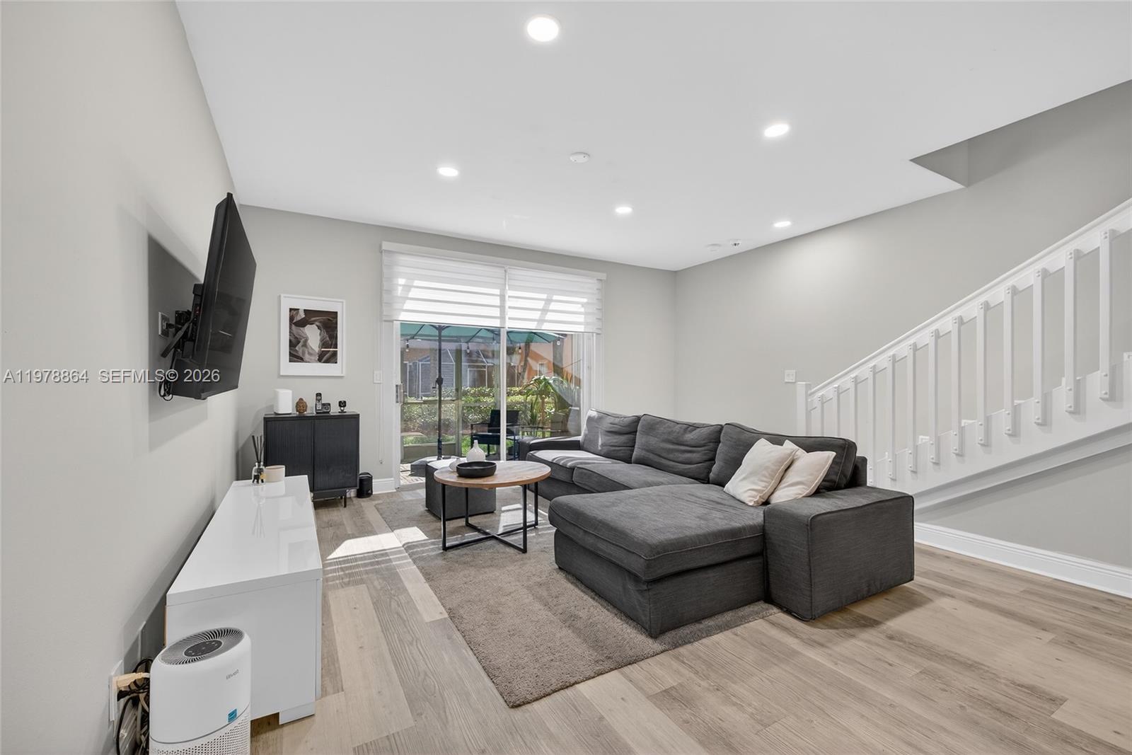 A living room features a gray sectional sofa, a white media console, and a staircase — 1594 Barcelona Way # 18, Weston FL 33327, WESTON, FL