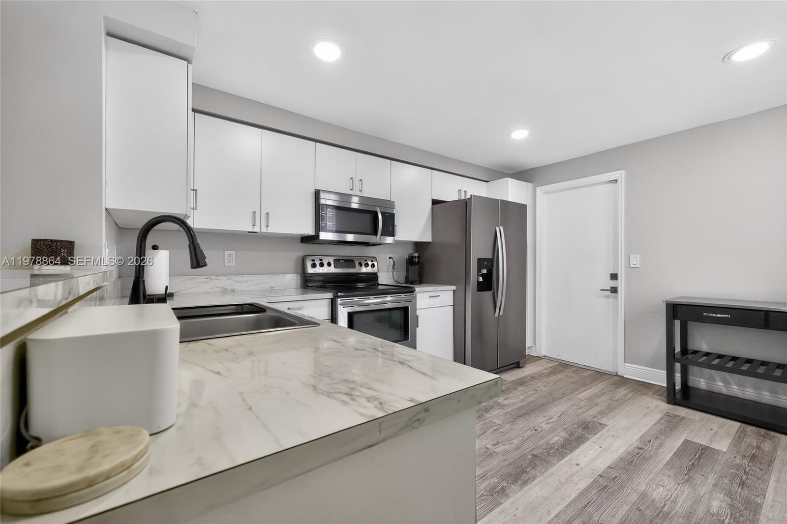 A kitchen features white cabinets, stainless steel appliances, marble-look countertops, and wood-style flooring — 1594 Barcelona Way # 18, Weston FL 33327, WESTON, FL