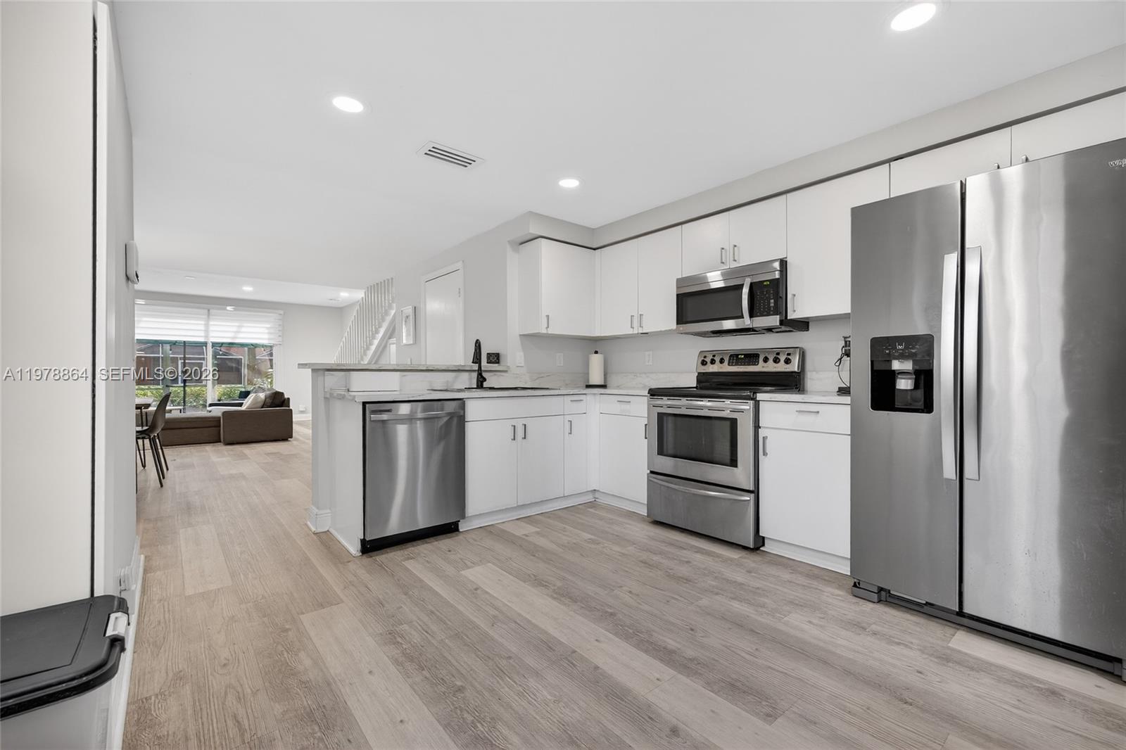 A modern kitchen features white cabinets, stainless steel appliances, and light wood-look flooring — 1594 Barcelona Way # 18, Weston FL 33327, WESTON, FL