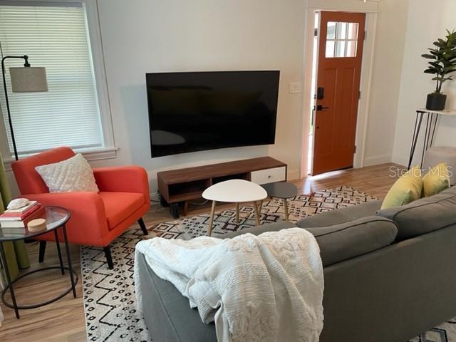 A living room features a grey sofa, an orange armchair, a wall-mounted television, and a door — 3646 6TH AVENUE N, ST PETERSBURG, FL