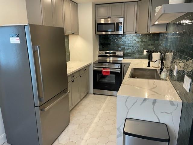 A modern kitchen features gray cabinets, stainless steel appliances, a marble countertop, and green tile backsplash — 3646 6TH AVENUE N, ST PETERSBURG, FL