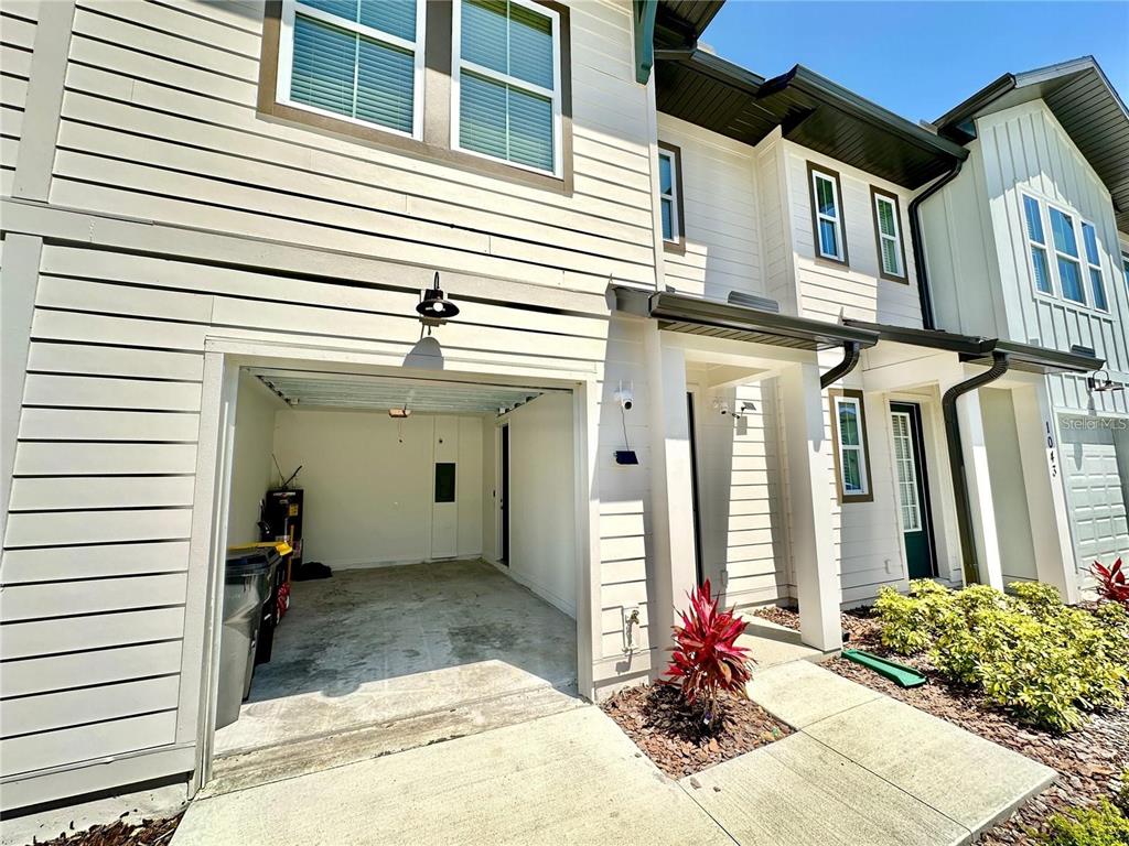 A two-story townhouse exterior features a single-car garage, a covered entryway, and light-colored siding — 1047 PLANTATION LANE, DAVENPORT, FL
