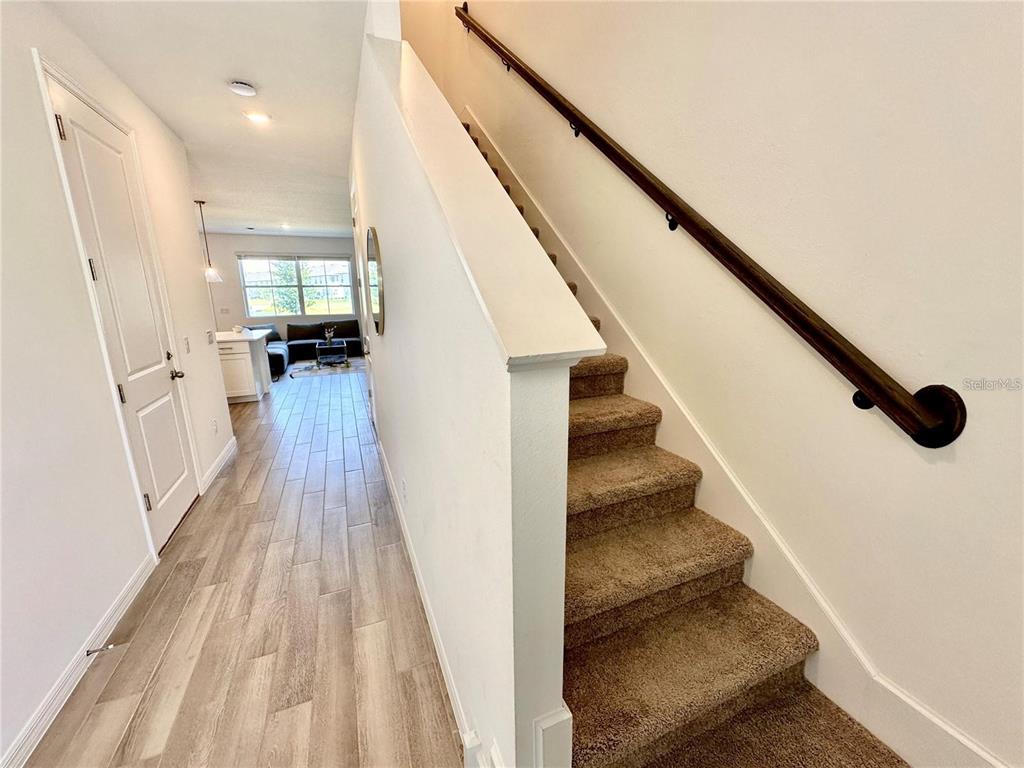 A hallway with wood-look tile flooring leads to a living area past a carpeted staircase — 1047 PLANTATION LANE, DAVENPORT, FL