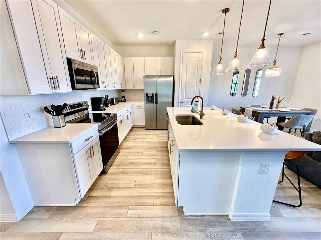 A modern kitchen features white cabinetry, quartz countertops, stainless steel appliances, and a central island — 1047 PLANTATION LANE, DAVENPORT, FL
