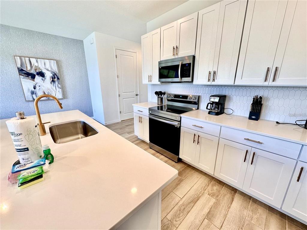 A modern kitchen features white cabinets, quartz countertops, a center island, and stainless steel appliances — 1047 PLANTATION LANE, DAVENPORT, FL
