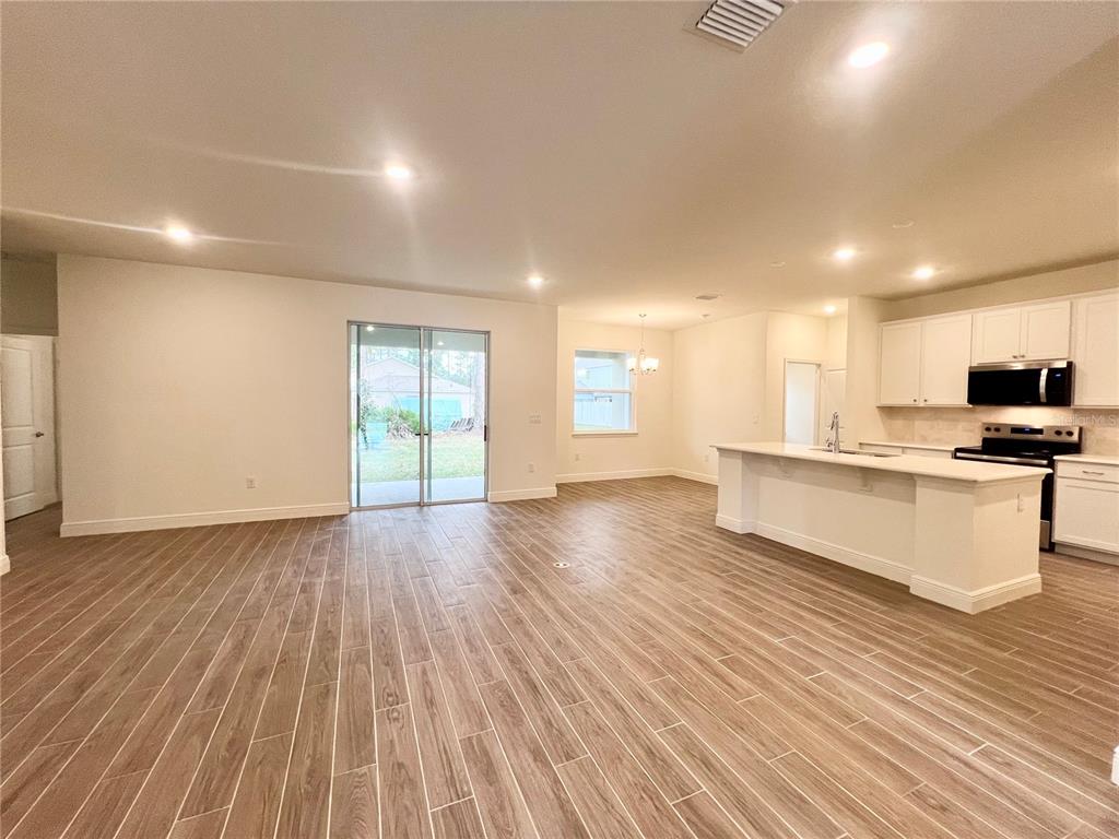 An open-concept kitchen and living area features white cabinetry, a center island, and wood-look flooring — 1 SEA FLOWER PATH, PALM COAST, FL
