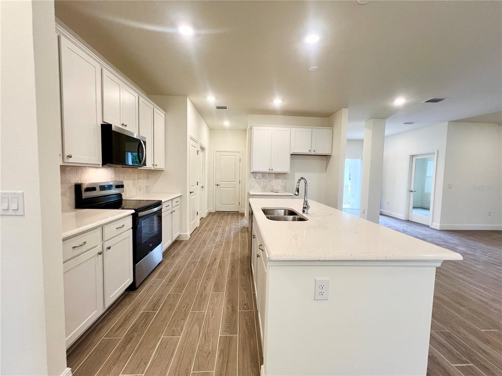 A kitchen features white cabinets, stainless steel appliances, a center island, and wood-look tile flooring — 1 SEA FLOWER PATH, PALM COAST, FL