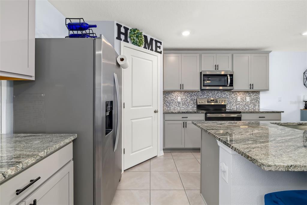 A kitchen features gray cabinets, stainless steel appliances, granite countertops, and a tiled backsplash — 17315 WHEATBERRY BOULEVARD, PARRISH, FL