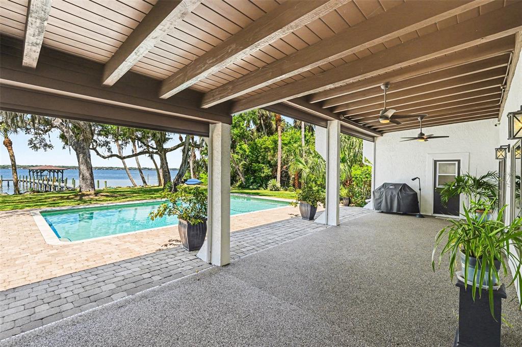 A covered patio with a textured floor overlooks a swimming pool and a waterfront view — 4137 CROOKED MILE ROAD, MERRITT ISLAND, FL