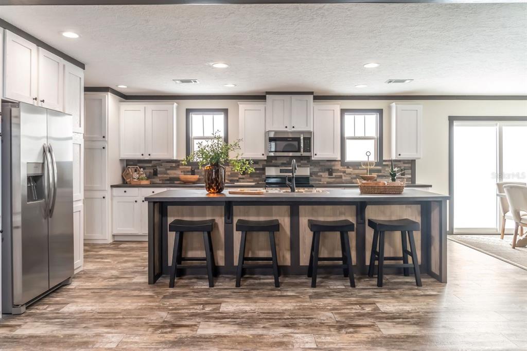 A modern kitchen features white cabinetry, a dark island with four stools, and wood-look flooring — 18088 NW 304TH STREET, OKEECHOBEE, FL