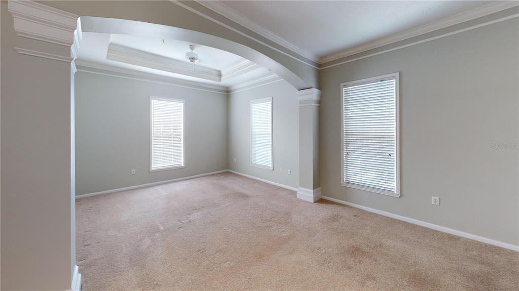 An empty room with beige carpet, light walls, and a tray ceiling with an archway — 235 GOLDENRAIN DRIVE UNIT 303, CELEBRATION, FL