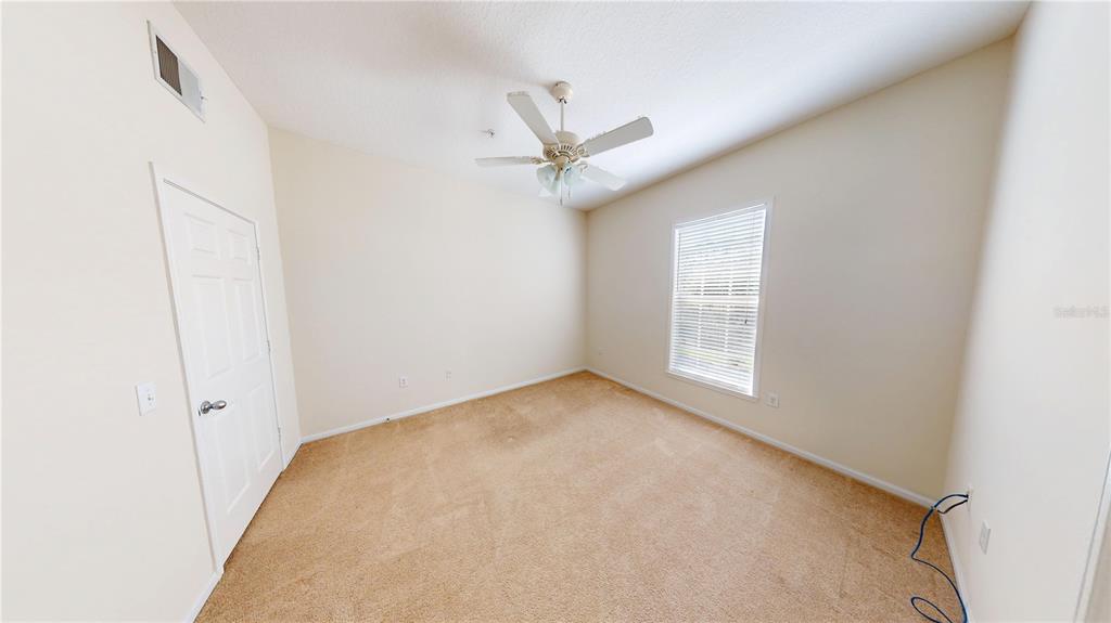 An empty bedroom features beige carpet, cream walls, a ceiling fan, and a single window — 235 GOLDENRAIN DRIVE UNIT 303, CELEBRATION, FL
